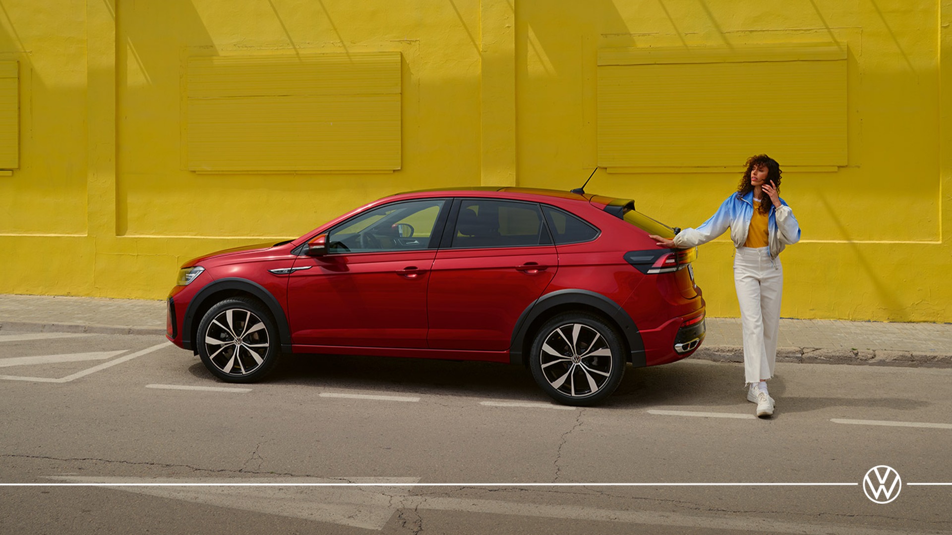 A woman leans against a red Volkswagen Taigo